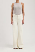 Woman wearing light gray sleeveless top paired with high-waisted, wide-leg white denim jeans, showcasing modern casual fashion.