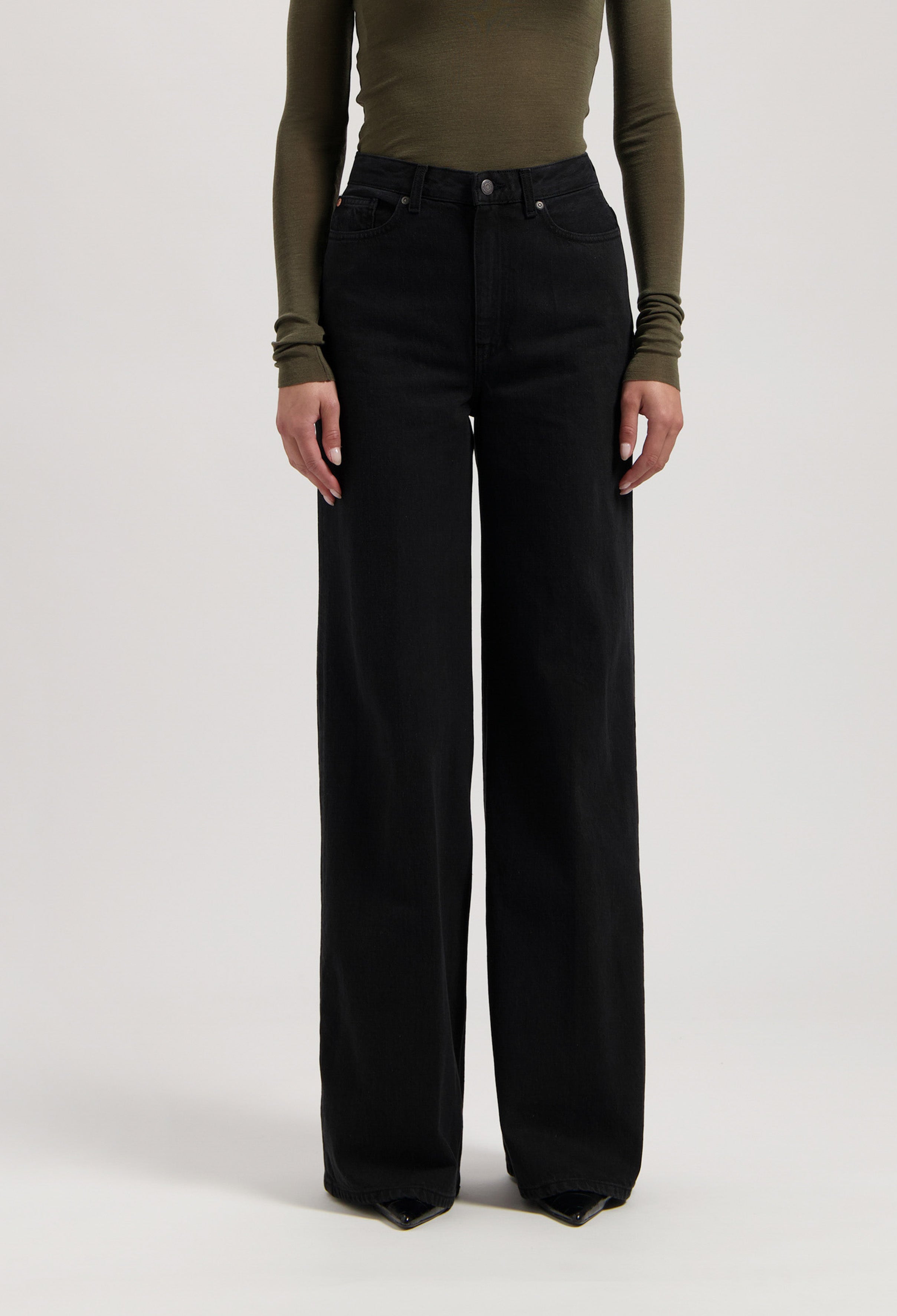Woman wearing high-waisted, wide-leg black denim jeans paired with an olive green, long-sleeve fitted top.