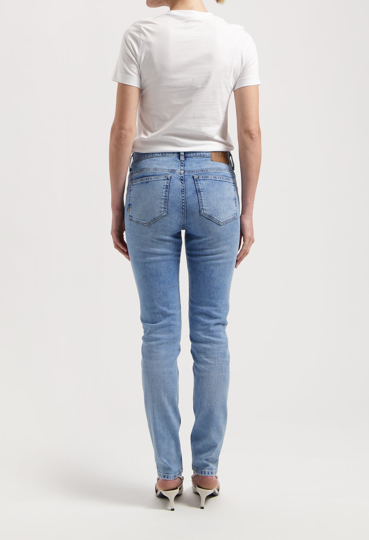 Back view of light blue denim jeans paired with a simple white T-shirt, worn by a model standing in heels.