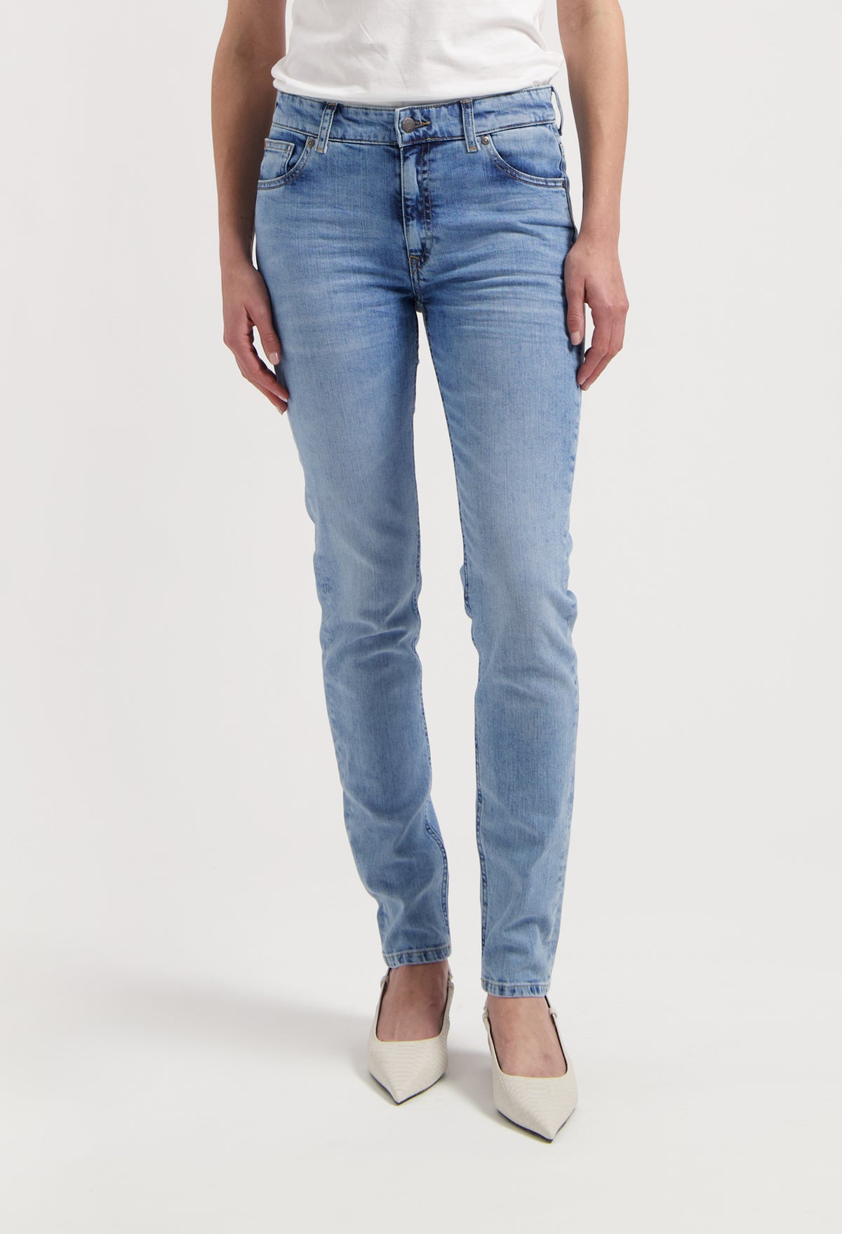 Light blue slim-fit jeans made from denim, paired with a white top and pointed white heels, showcased on a person standing.