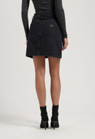 Dark denim skirt with back pockets paired with a long-sleeve gray top and black high-heeled ankle boots.