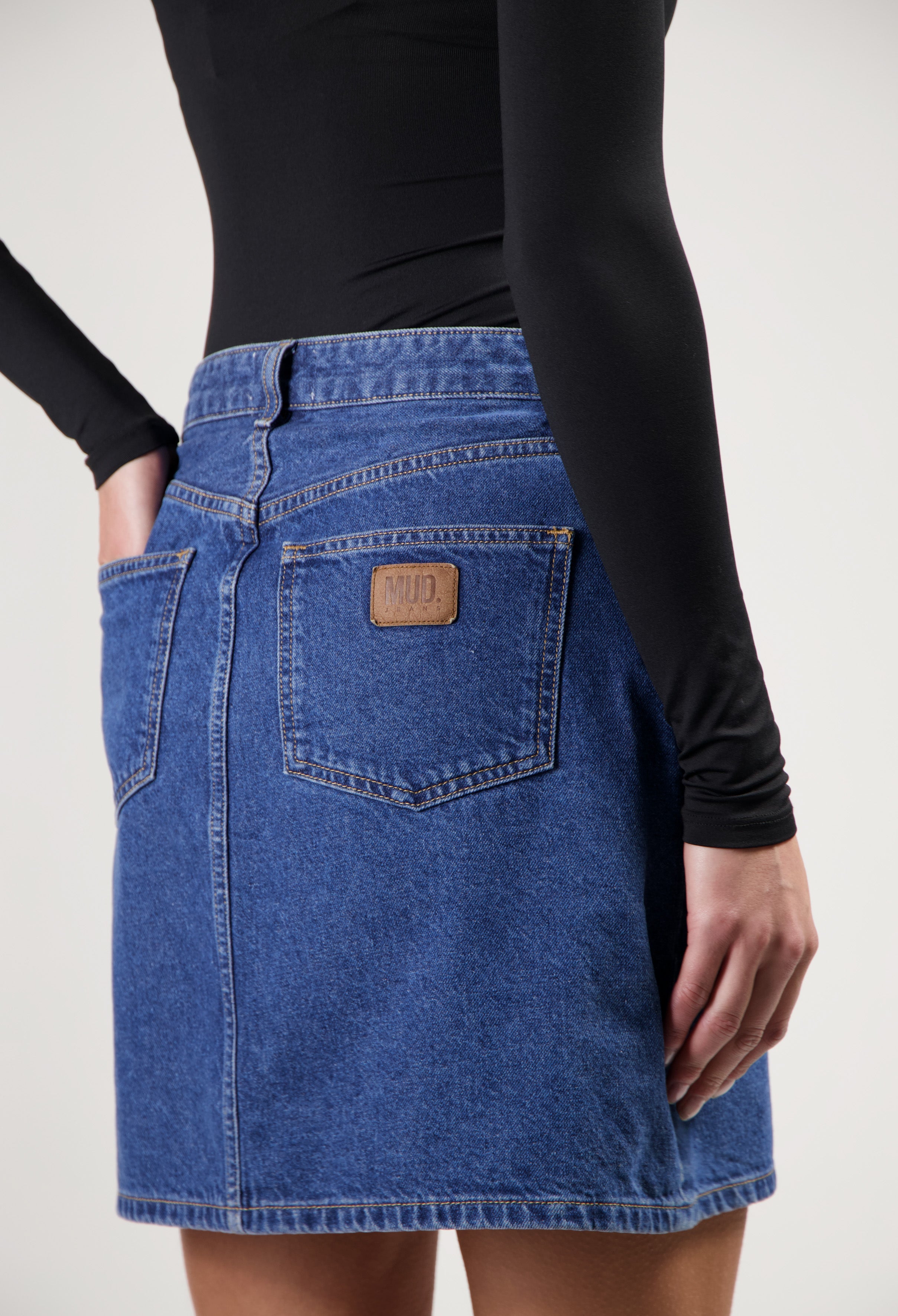 Sustainable blue denim skirt by MUD Jeans, featuring deep blue fabric, back pockets, and paired with a fitted black top.