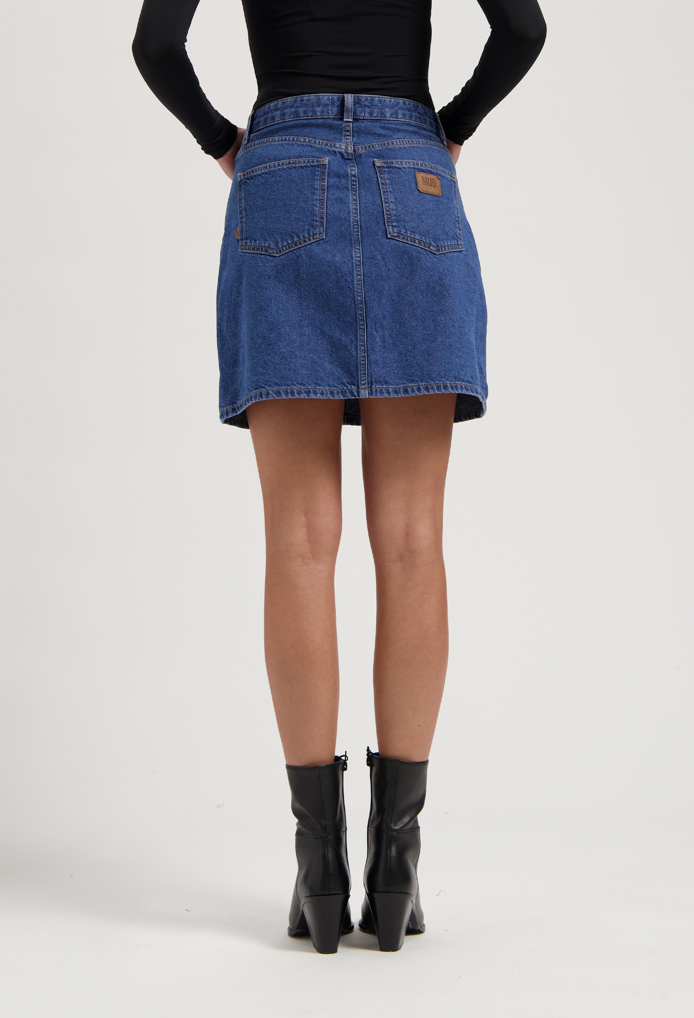 Denim A-line skirt in blue from MUD Jeans, paired with black leather ankle boots and a fitted long-sleeve black top.