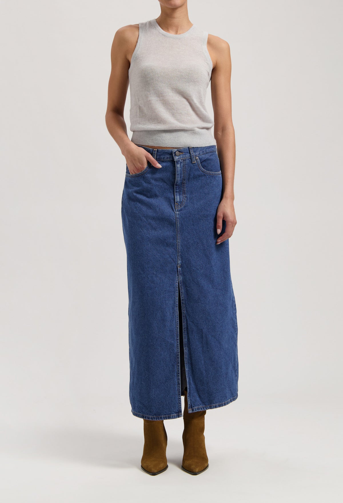 Long blue denim skirt with front slit, paired with a sleeveless gray top and brown pointy boots, showcasing casual chic style.