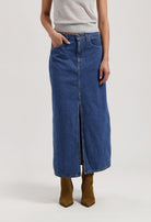 Woman wearing a long denim skirt with front slit, paired with a sleeveless gray top and brown suede ankle boots.