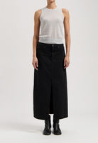 Model wearing a sleeveless gray top with a long black denim skirt, featuring a central slit, and black ankle boots.