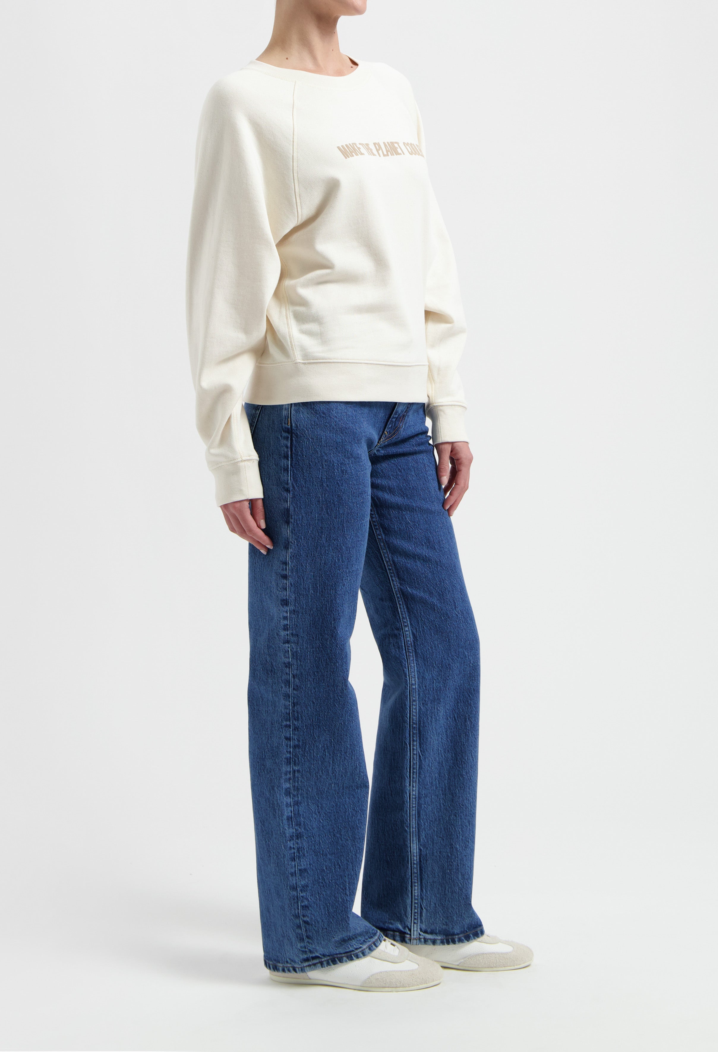 Woman modeling a cream sweatshirt with blue wide-leg jeans and white sneakers, showcasing casual and comfortable fashion.