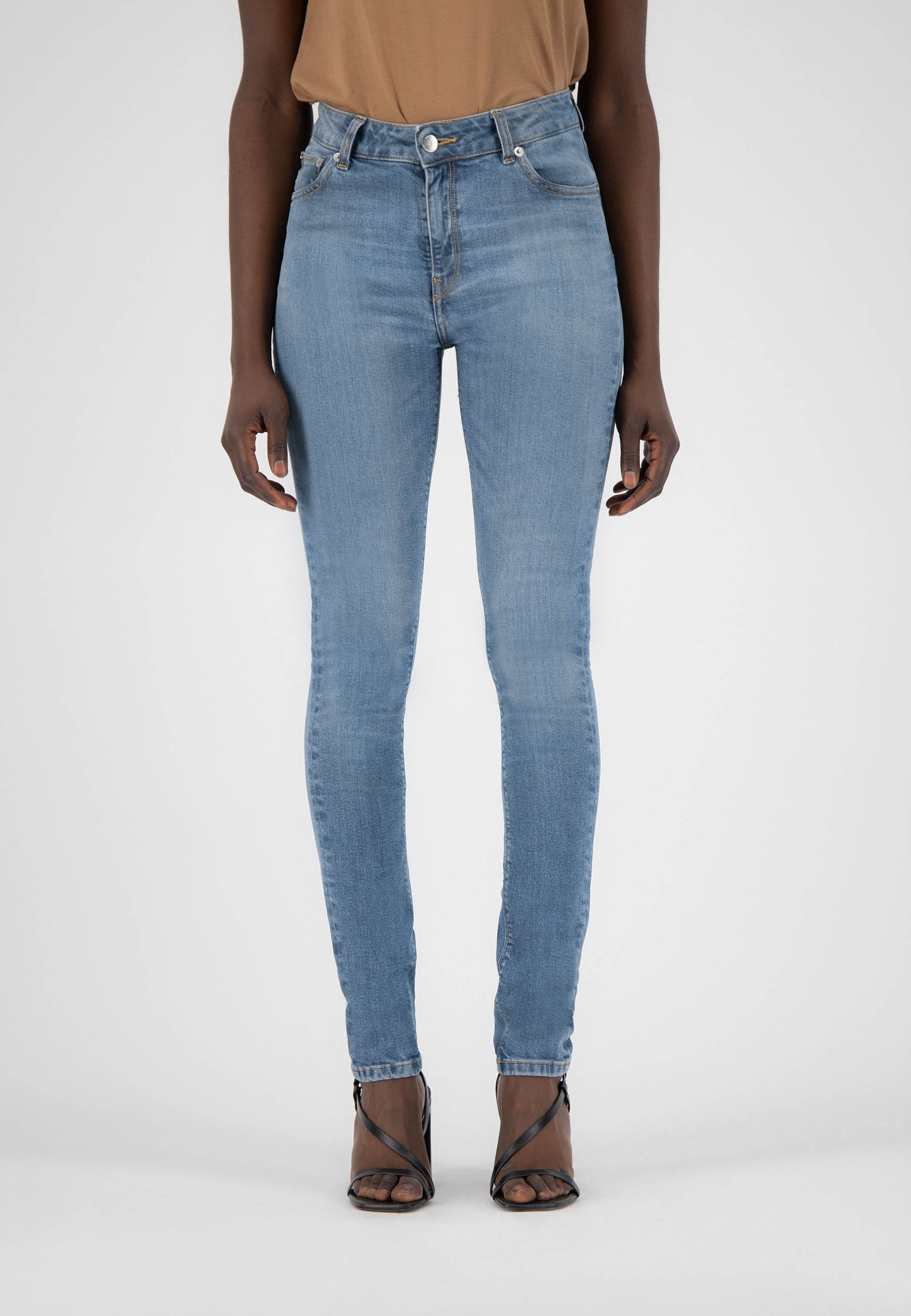 Light blue high-waisted skinny jeans worn with a beige sleeveless top and black strappy heels on a plain background.