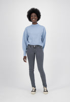 Person wearing a light blue sweater with puffed sleeves and fitted gray jeans, paired with black and white sneakers.